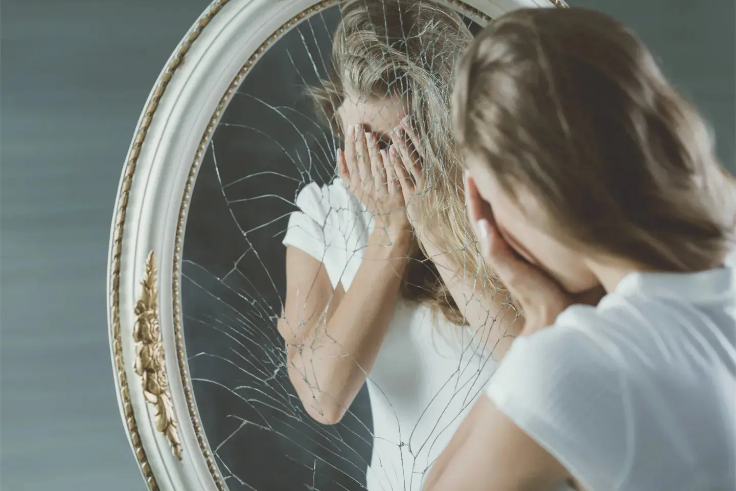 girl is hiding her face visible in a broken mirror